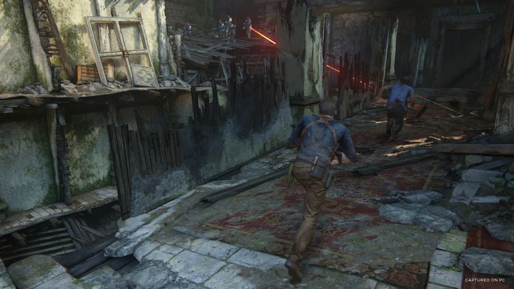 Scene from Uncharted: Legacy of Thieves Collection showing characters escaping a ruined building with lasers.