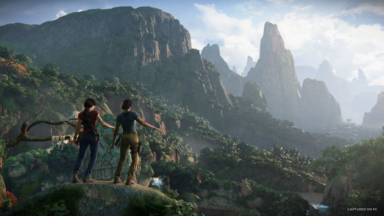 Two characters stand on a cliff overlooking a lush, mountainous landscape in Uncharted: Legacy of Thieves Collection.
